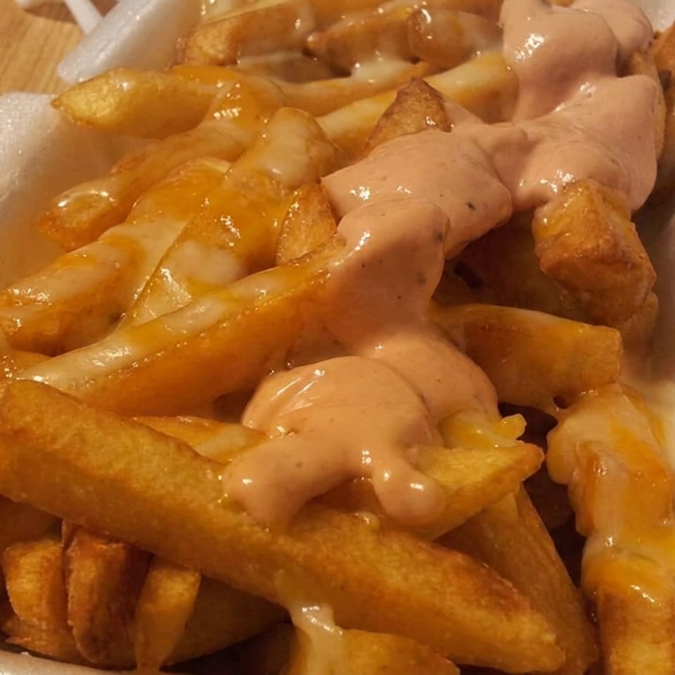 Crispy fries in a foam container drizzled with orange cheese sauce and creamy pink dressing.